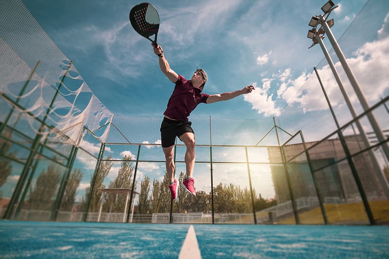 A young padel player jumps to hit the ball in an outdoor game. A young padel player jumps to hit the ball in an outdoor game.